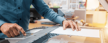 Ein Mitarbeiter bedient einen Multifunktionsdrucker und scannt ein Blat Papier ein.