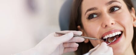 Eine Frau zeigt Ihre Zähne dem behandelten Zahnarzt. Deiser untersucht sie mit dem Mundspiegel.